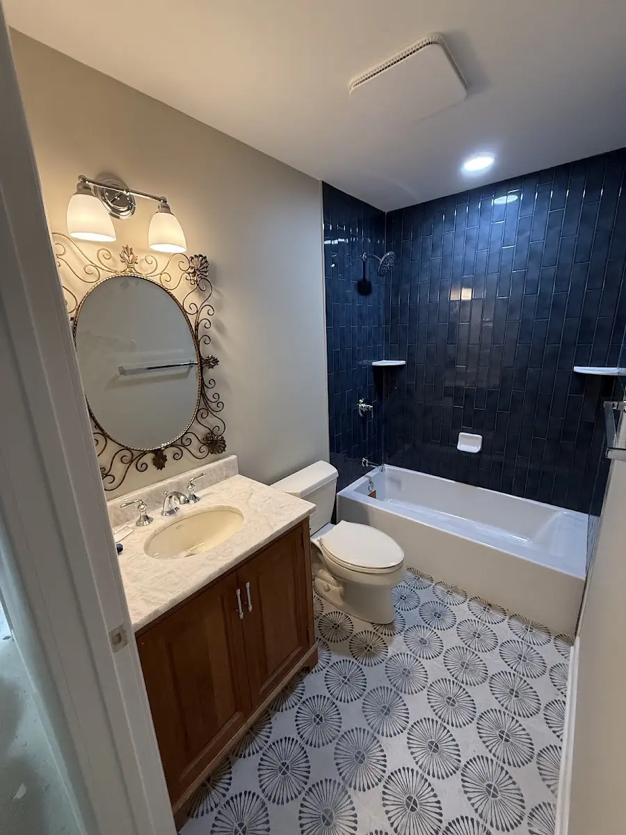 Completed bathroom remodel with glossy navy tile tub surround, patterned floor tile, wood vanity and decorative oval mirror
