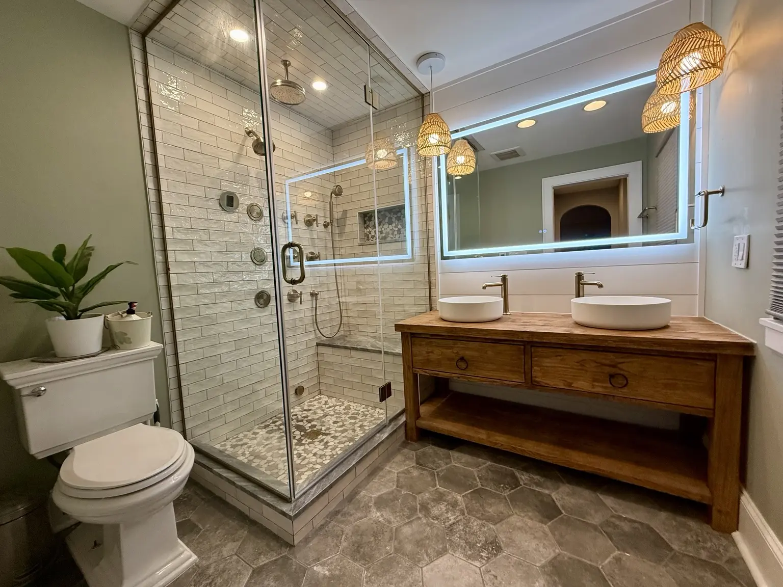 Completed bathroom remodel with a pebble-floored glass shower, double vessel vanity, subway tile and warm woven pendants
